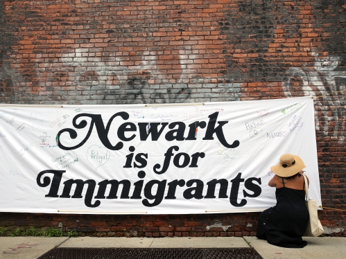 woman kneeling in front of "newark is for immigrants" banner